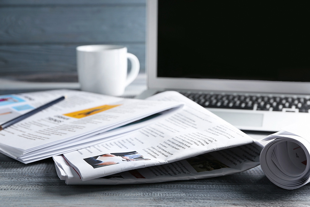 Newspapers, laptop and cup of coffee on table