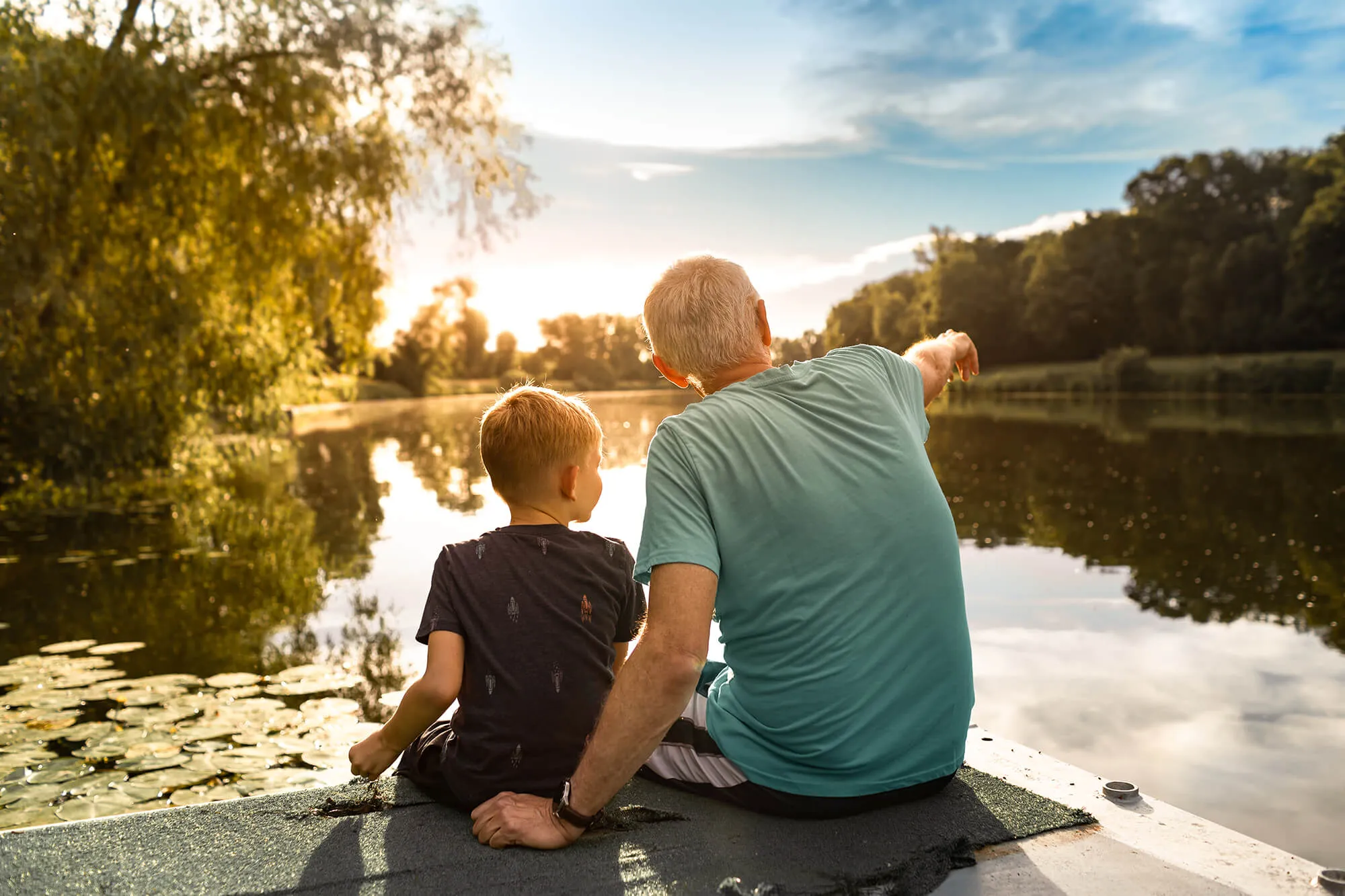 Grandfather and grandson sitting together outdoors on a dock by a lake